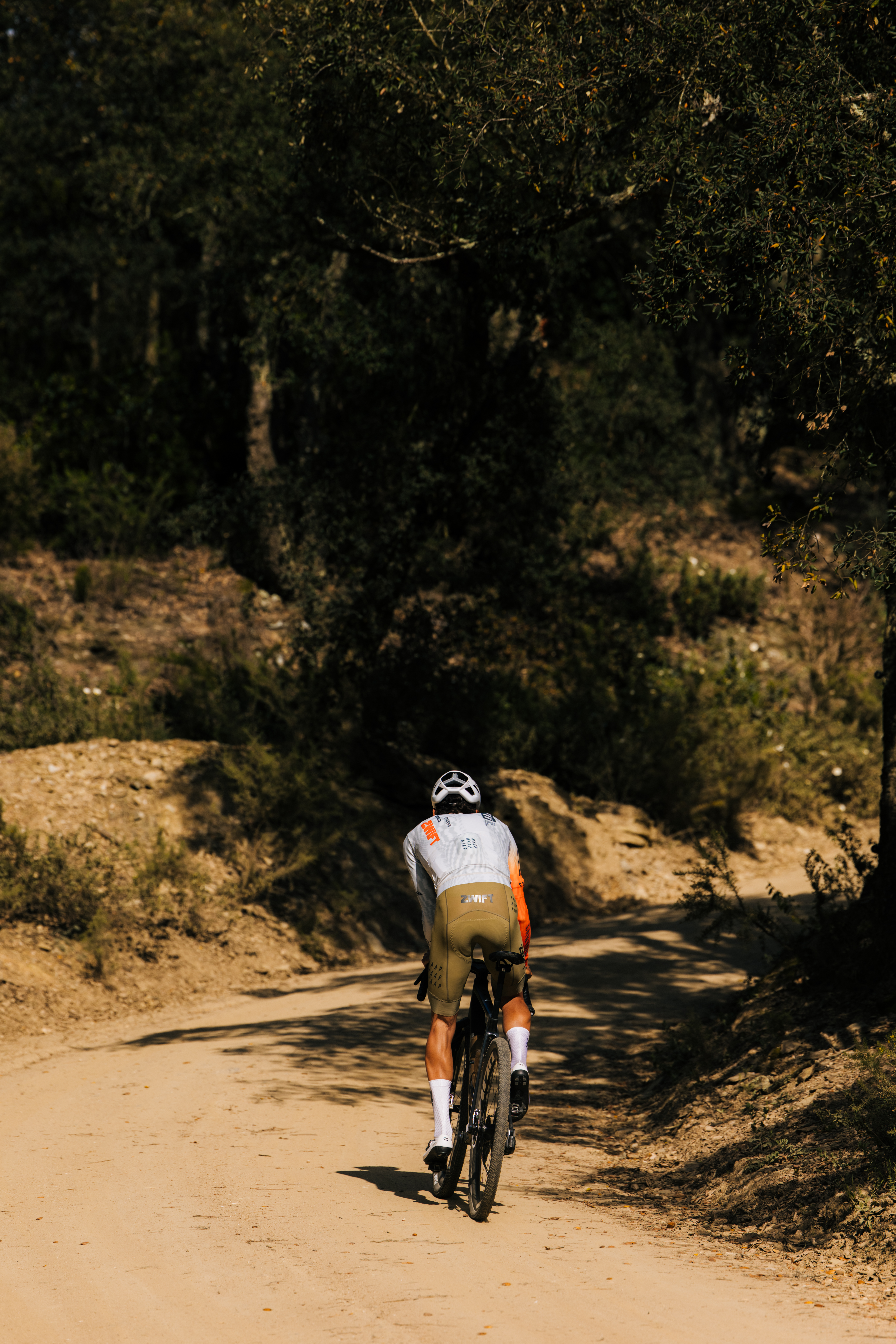 a cyclist riding up a climb on a gravel road, viewed from behind
